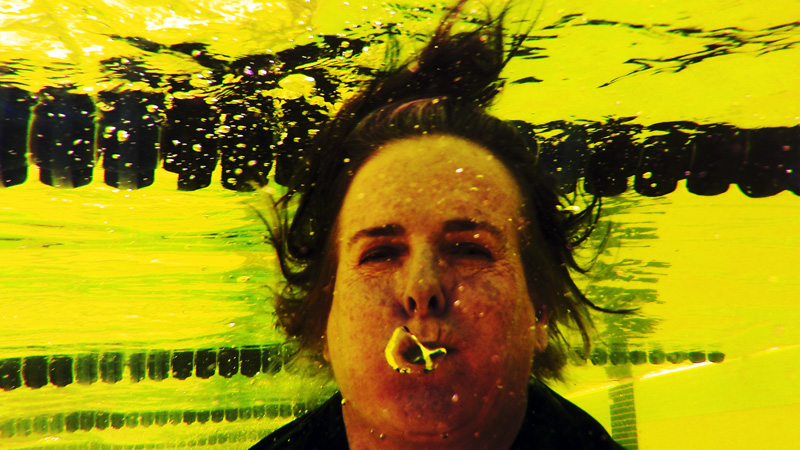 Janet Gibson in yellow light underwater, her hair floating above her head like a medusa, her mouth open